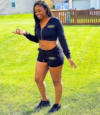 a woman in black shorts and a hoodie standing in a grassy area