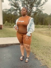 a black woman in a tan romper posing in front of a house