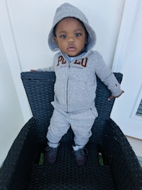 a baby sitting on a chair in a grey hoodie and sneakers