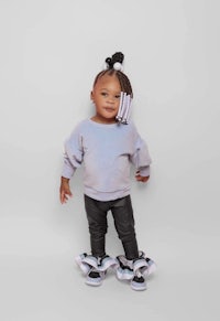 a baby girl wearing a grey sweatshirt and black leggings