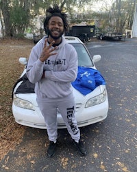 a black man standing next to a white car