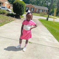 a young girl in a pink dress standing on a sidewalk